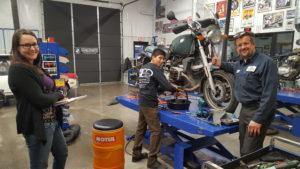 Monica from Inspire and Marc Beyer from OCD Custom Cycles & Auto Repair watching Alexis Flores working.